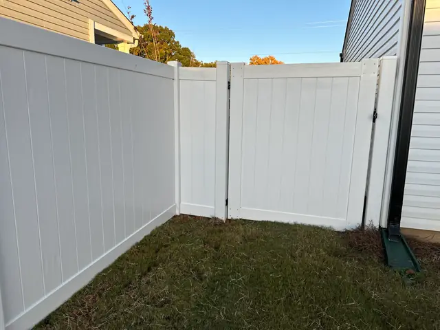 White vinyl privacy fence corner with a gate between two houses.