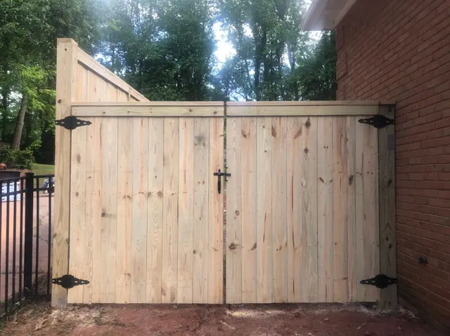 Wood double drive gate with black decorative hinges.