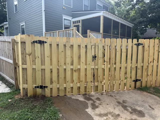 Wood double drive gate with spaced boards and black decorative hinges.