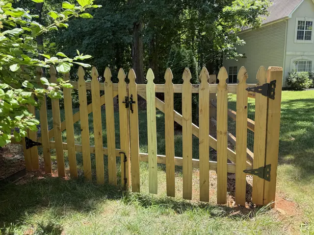 Wood picket gate with pointed pickets and black strap hinges.
