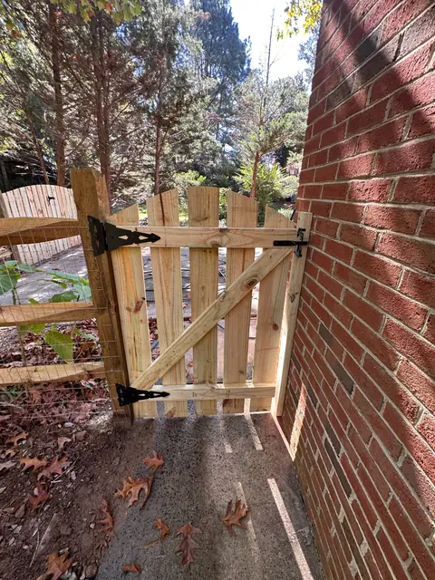Wood picket walk gate with black strap hinges next to a brick house.