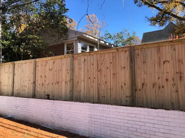Wood privacy fence with cap and trim on top of a painted brick retaining wall.