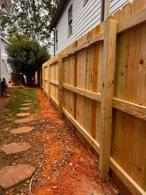 Back side of a wood privacy fence showing posts and three rails along a stepping stone path.