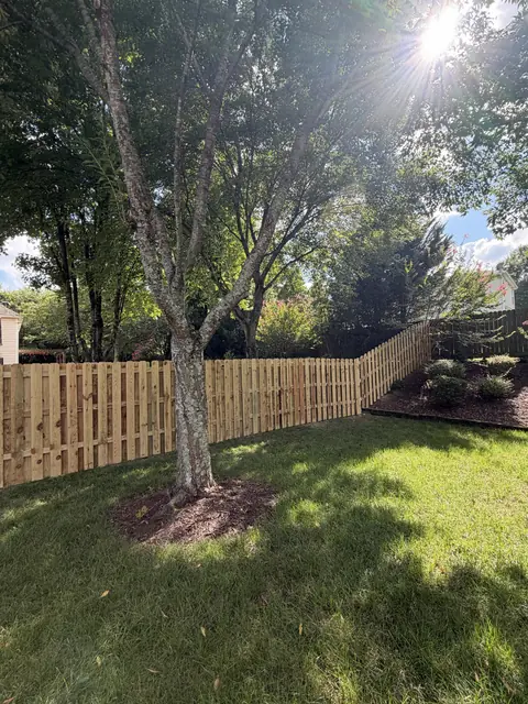 Wood semi-privacy fence with spaced boards stepping up a slope behind a tree.